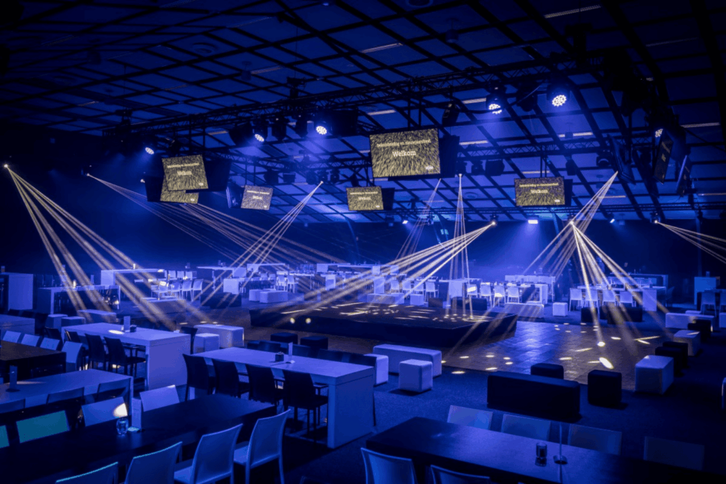 Groots opgezette zaal met lichtshow en tafelinrichting voor bedrijfsevent.