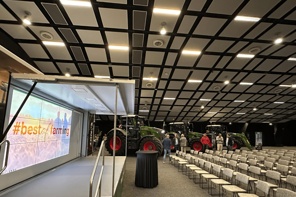 Evenementenzaal met podium en rijen stoelen klaar voor een tractorvoorstelling bij De Montil