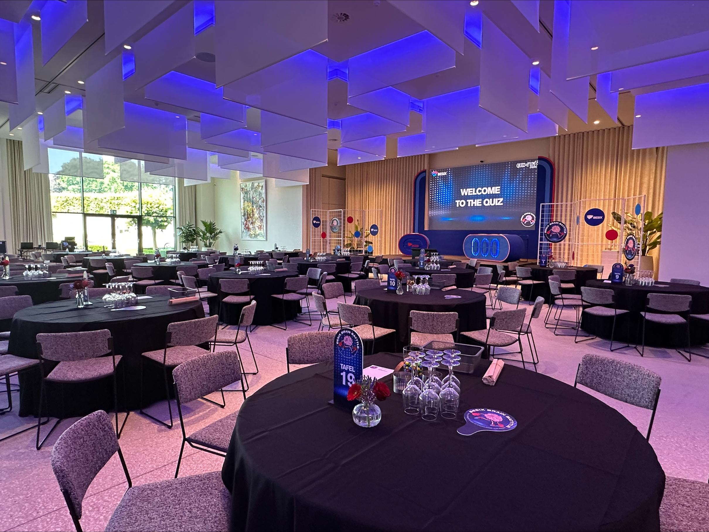 Stijlvolle eventzaal met tafels en groot scherm voor een interactieve quiz tijdens een personeelsfeest.