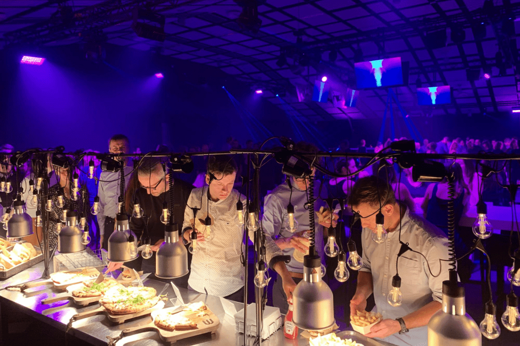 Medewerkers genieten van streetfood catering tijdens een sfeervol bedrijfsfeest met verlichting en muziek.